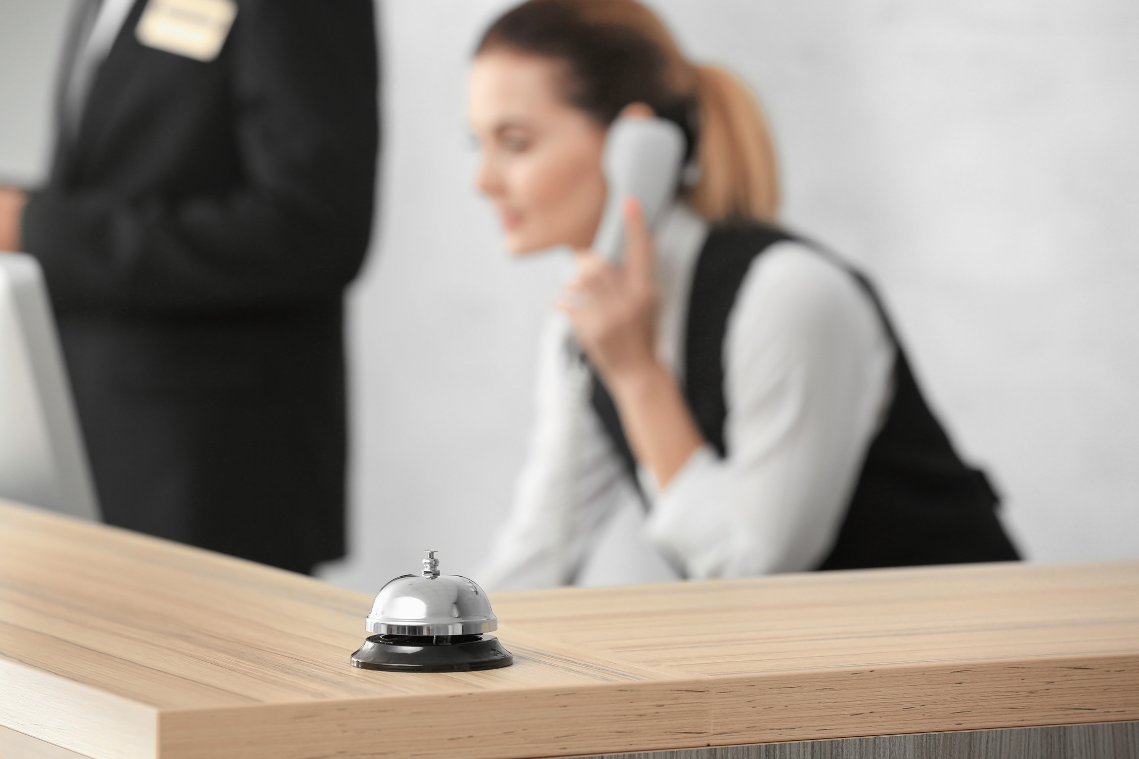 Service Bell on Desk and Blurred Female Receptionist in Hotel